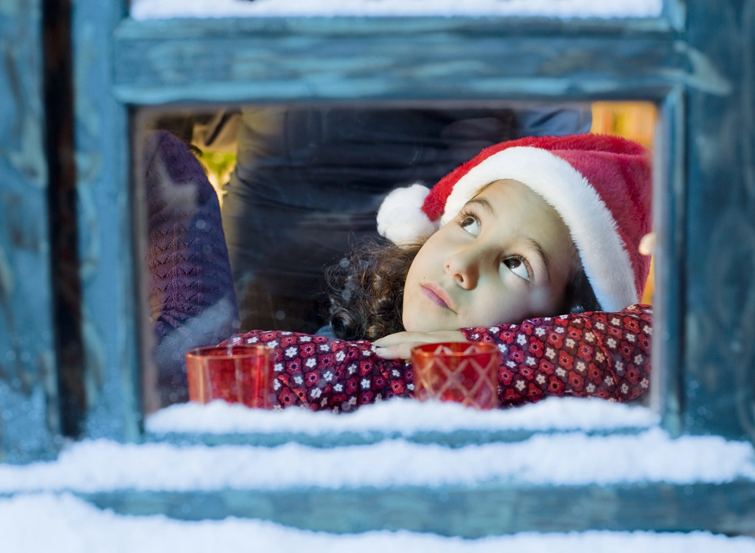 Kind schaut verträumt aus einem verschneiten Fenster zur Adventszeit