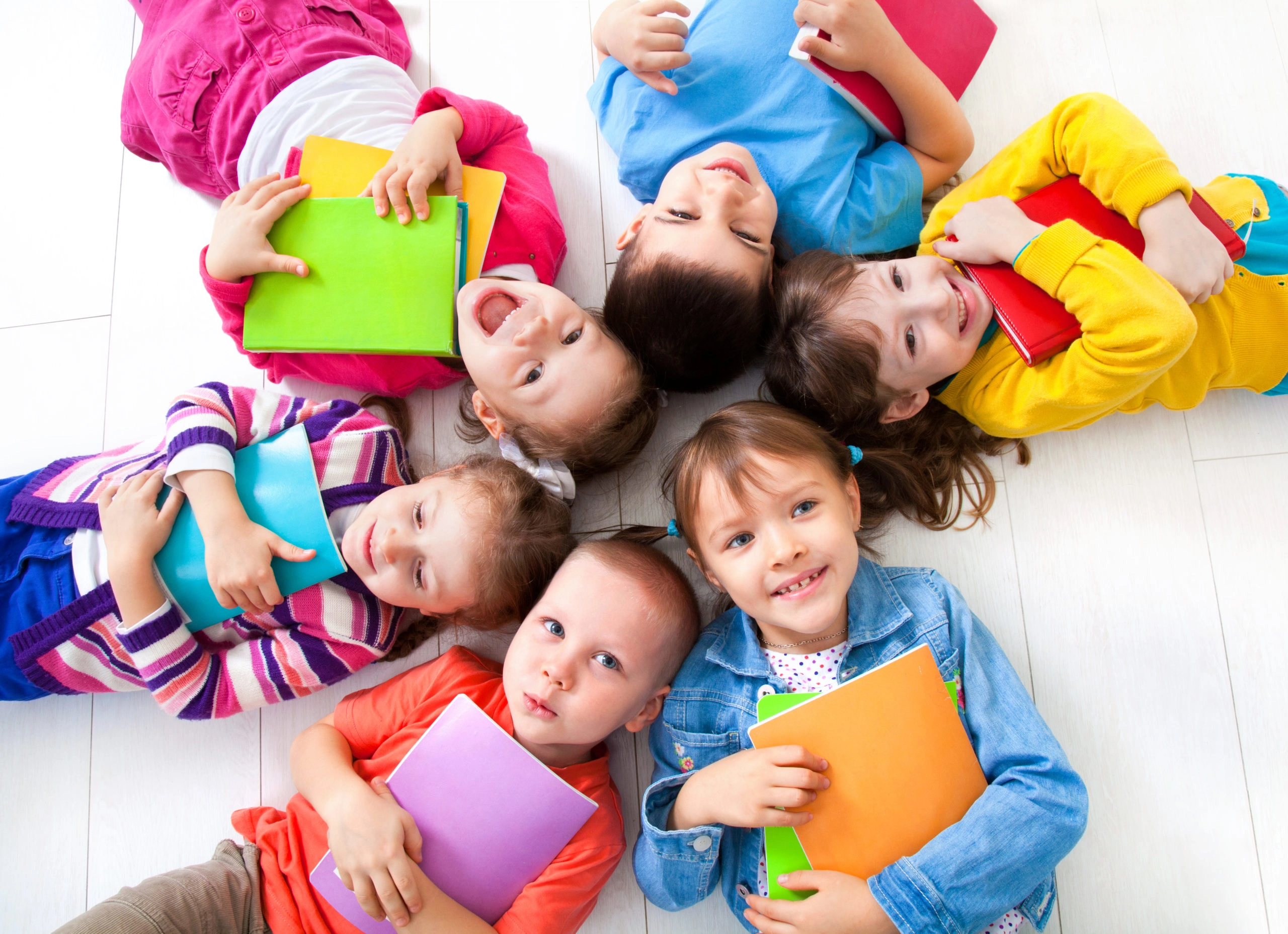 6 Kinder liegen Kopf an Kopf in einem Kreis mit Heften in den Händen zum entspannten Schulstart