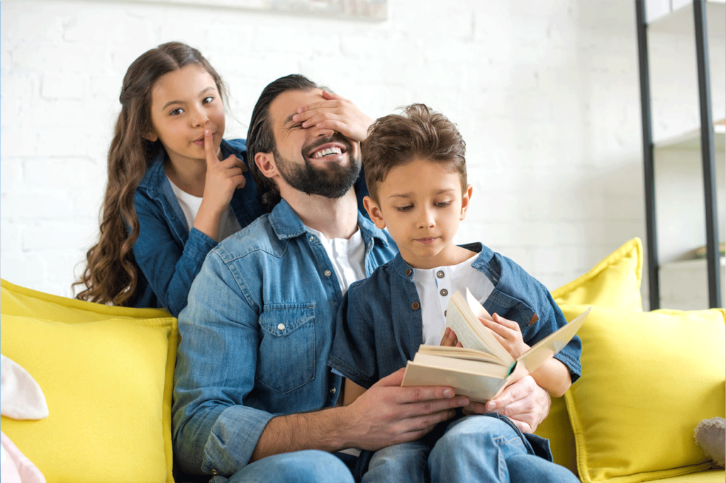 Vater beim Spielen und Lesen mit seinen zwei Kindern 