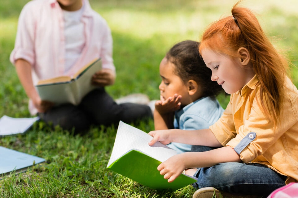 Gemeinsame Lesezeit bei den Kinder draußen auf einer Wiese
