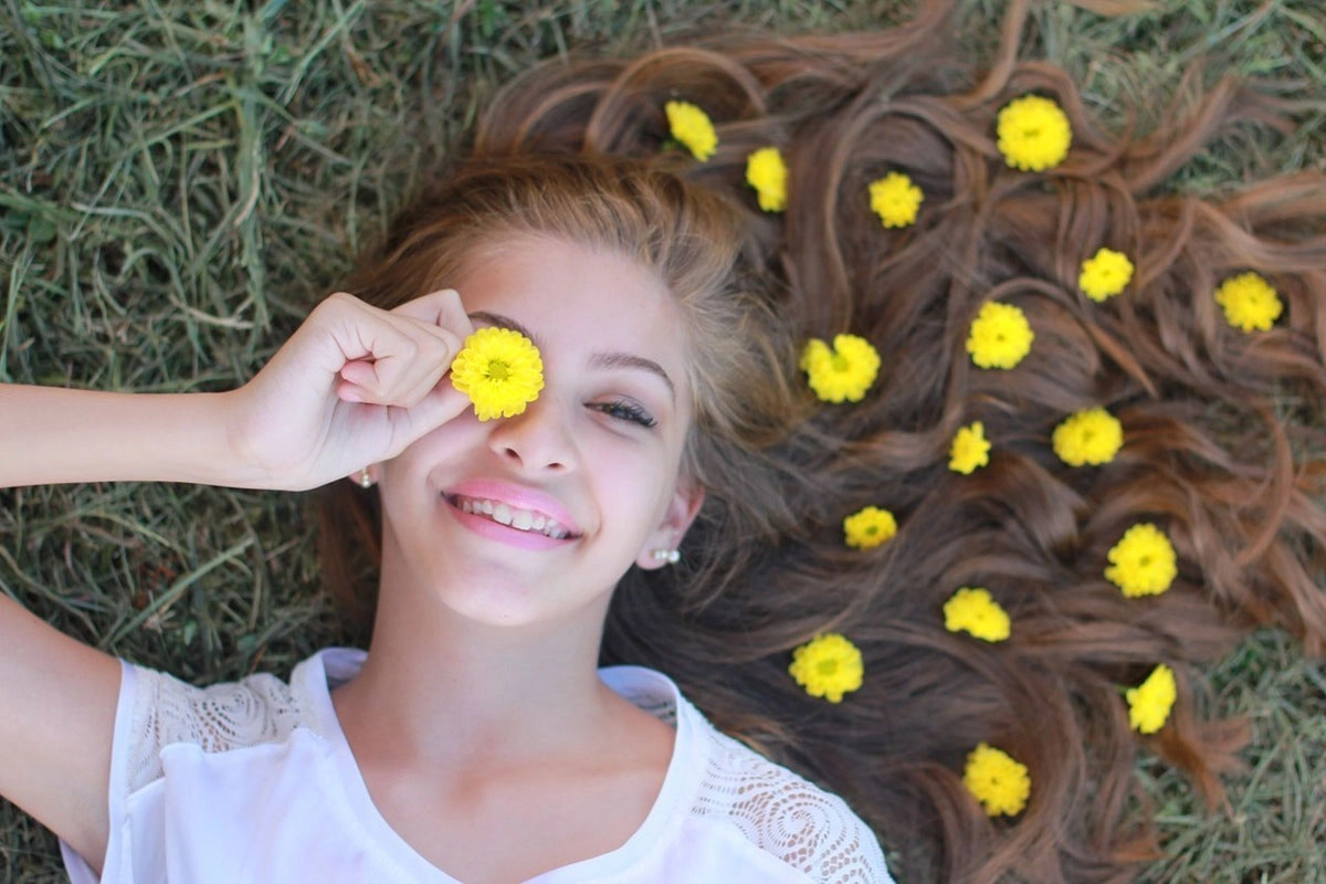 Junge Frau liegt mit gelben Blumen im Haar im Gras