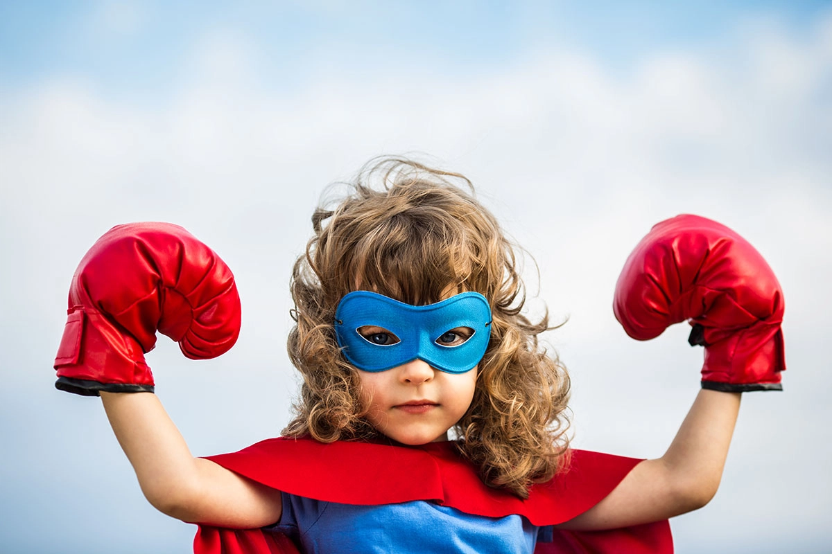 Mädchen mit Superman Kostüm und Boxhandschuhen gekleidet um Selbstvertrauen der Kinder aufzubauen